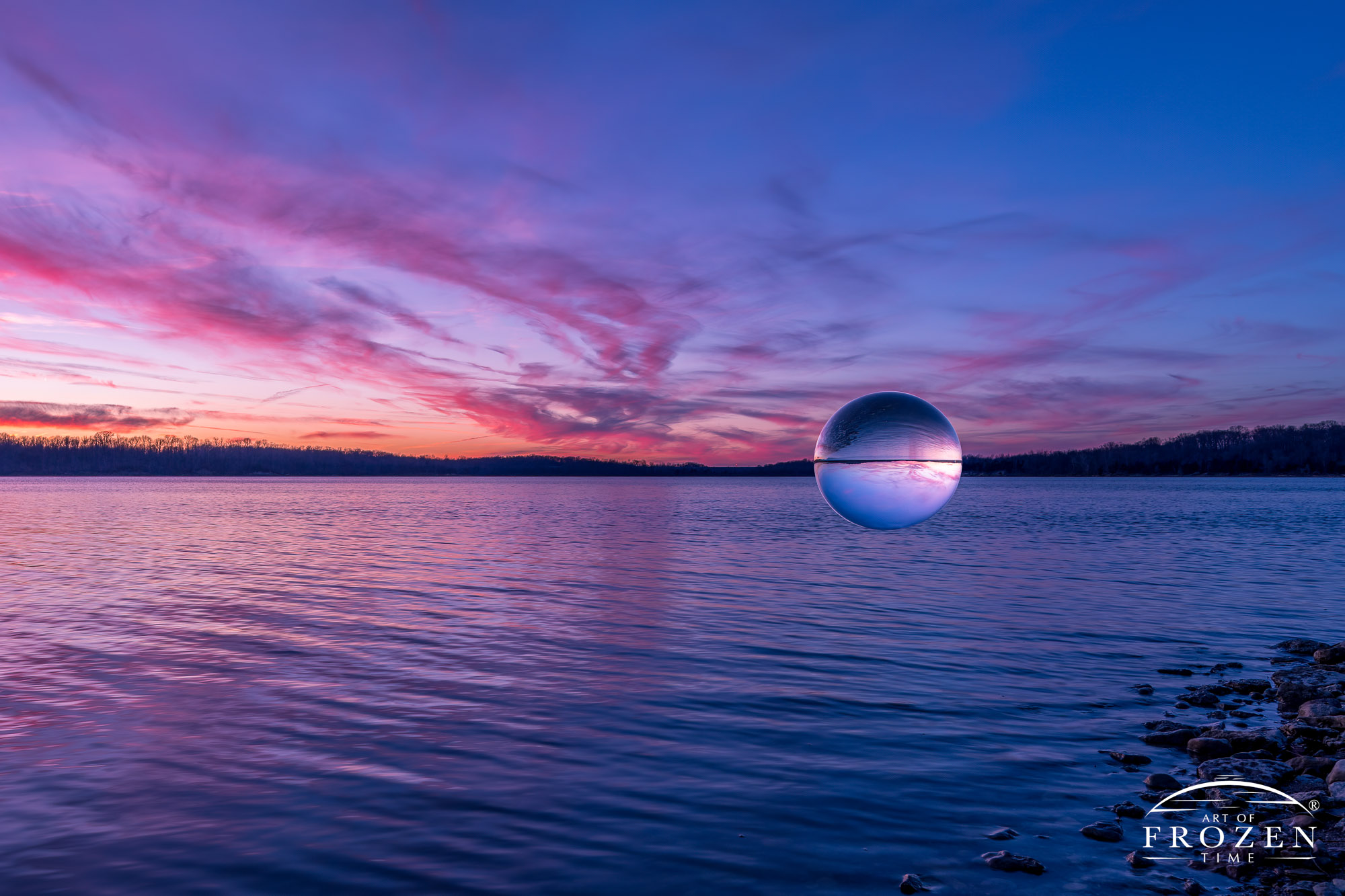 A crystal sphere held at eye level during a colorful sunset which inverts the impressive sky and the lake's surface
