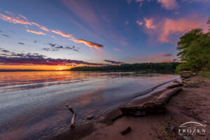 An evening sunset over Caesar Creek State Park where gentle waves wash ashore as overhead clouds catch colorful light.