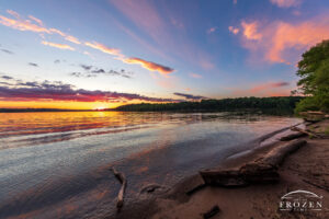 An evening sunset over Caesar Creek State Park where gentle waves wash ashore as overhead clouds catch colorful light.