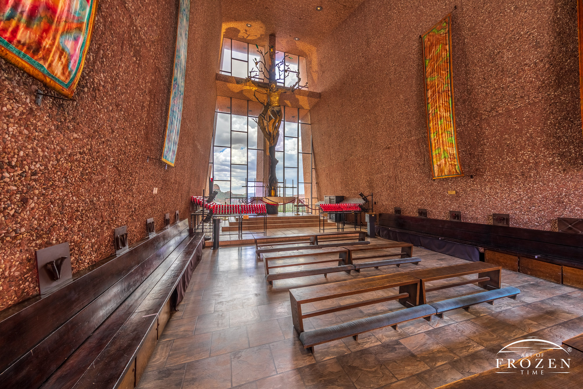 A wide-angle view of the Chapel of the Holy Cross interior revealing its textured walls leading the eye towards the church’s rear glass windows.