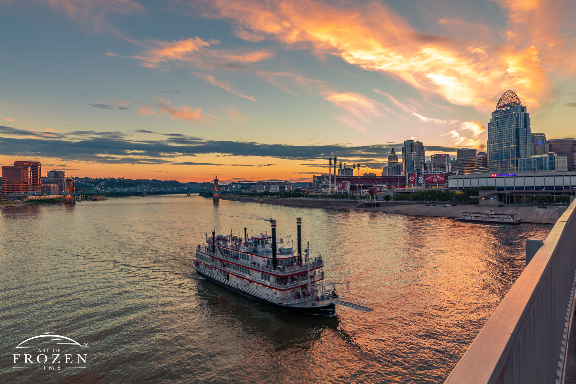 Ohio River Paddleboat powers its way by the Cincinnati Ohio skyline under colorful sunset skies.