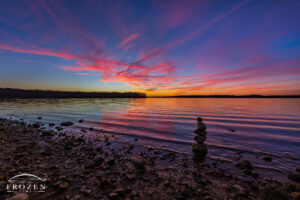 A colorful twilight along the shoreline of Caesar Creek State Park where gentle waves lap against the a rock cairn