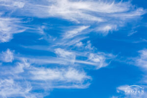 A view of wispy cirrus clouds being shaped by high altitude winds that below adjacent clouds into feathery streaks of vapor.