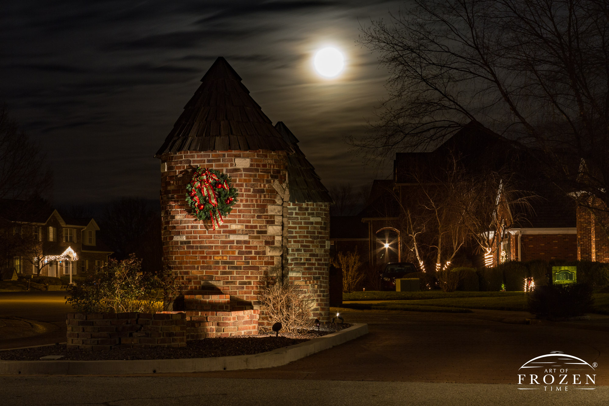 A tumbled brick monument at the entrance of an O’Fallon Illinois neighborhood where the December full moon rises over St. Clair County and landscape lights illuminate the holiday decorations.