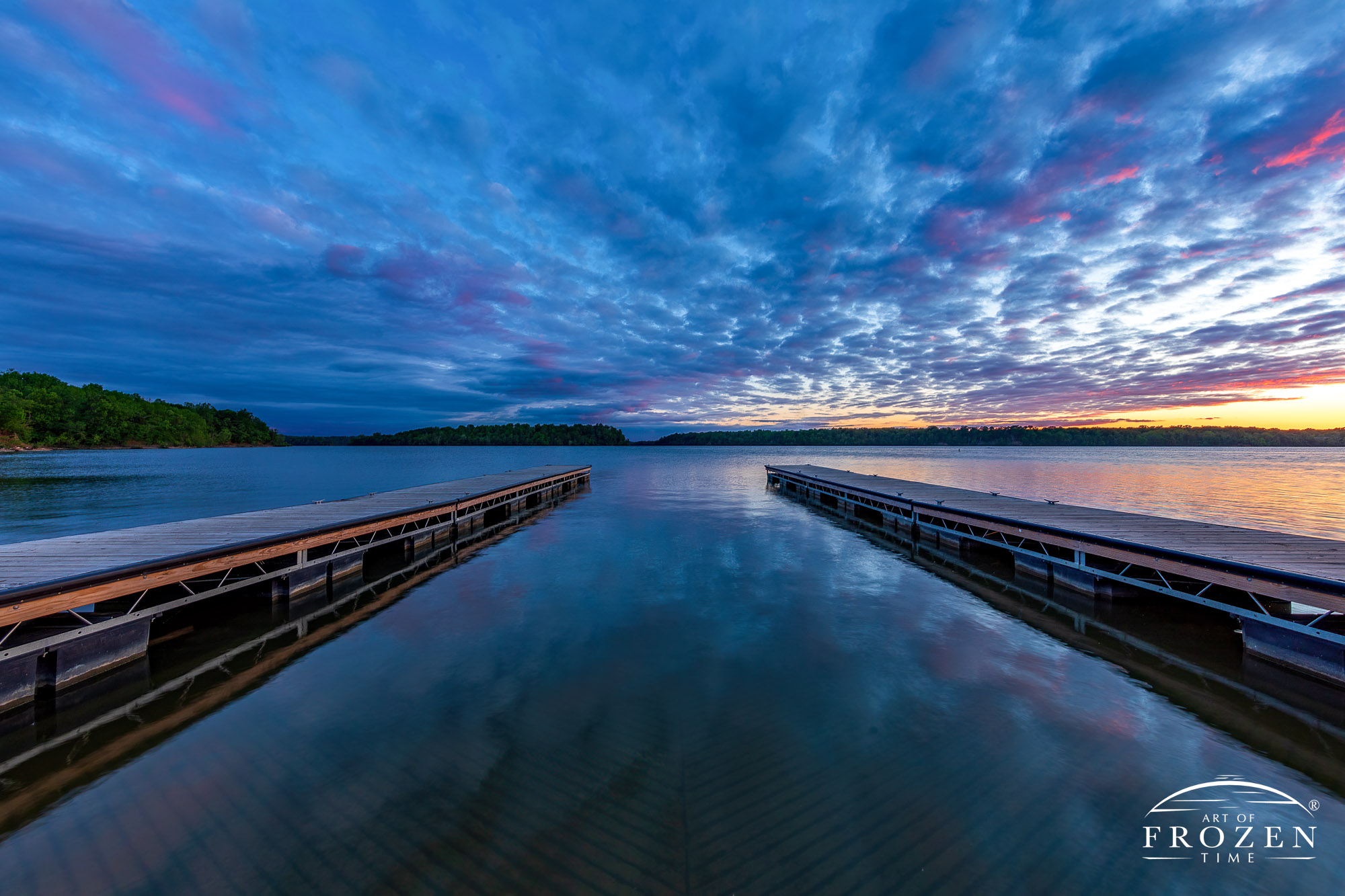 A colorful sunset over Caesar Creek State Park where the setting sun illuminated the parting clouds from underneath as twilight approached and two boat docks stretch outward into the calm waters.