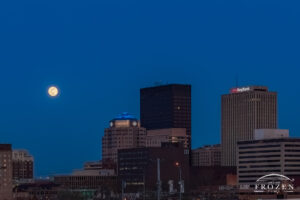 A twilight view of the Dayton Skyline with a full moon hanging above the the towers of Dayton, Ohio.