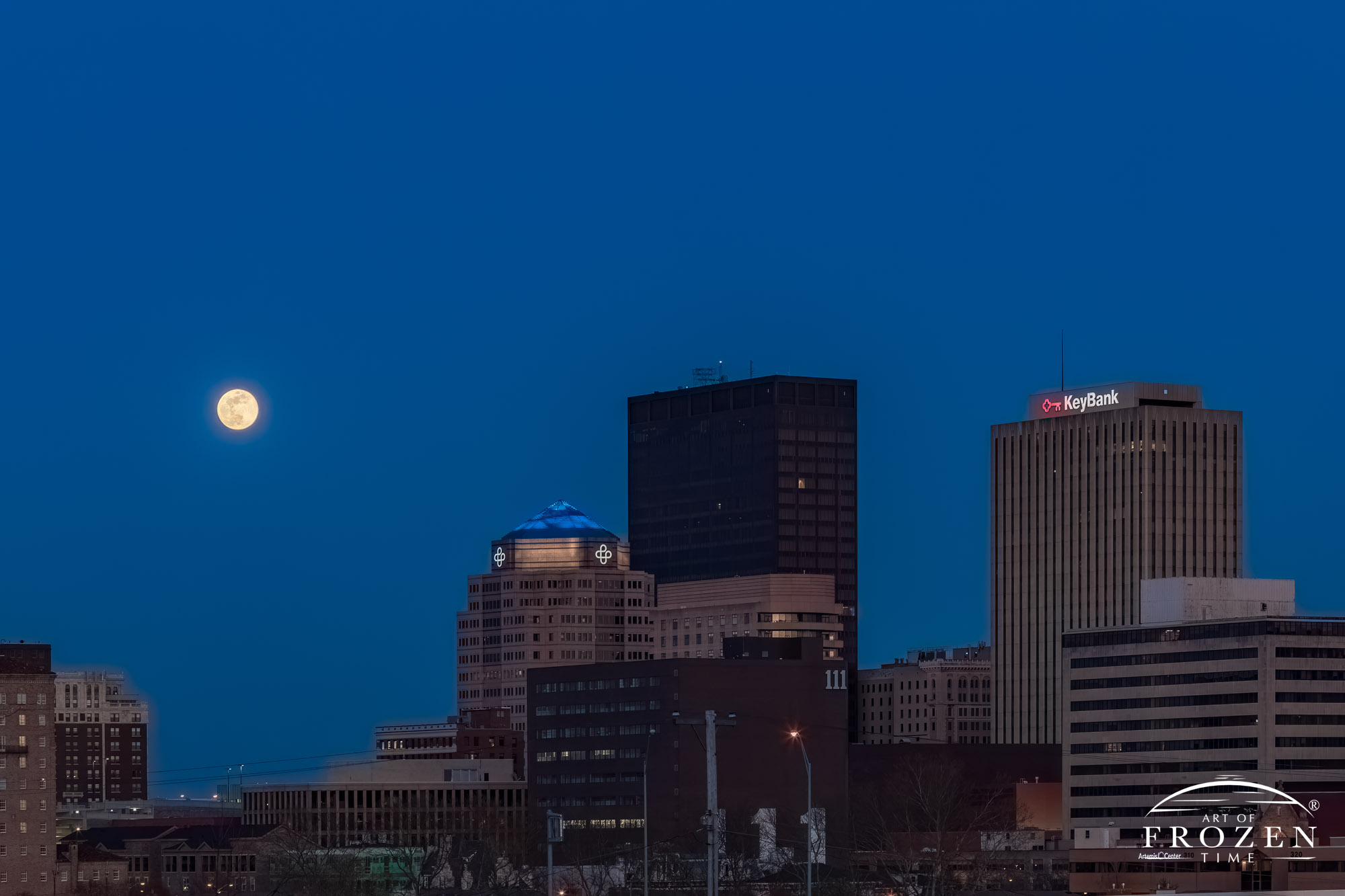 A twilight view of the Dayton Skyline with a full moon hanging above the the towers of Dayton, Ohio.