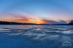A frozen lake surface during a winter sunset where twilight descends over Ohio as high cirrus clouds catch the last of the day in vivid colors