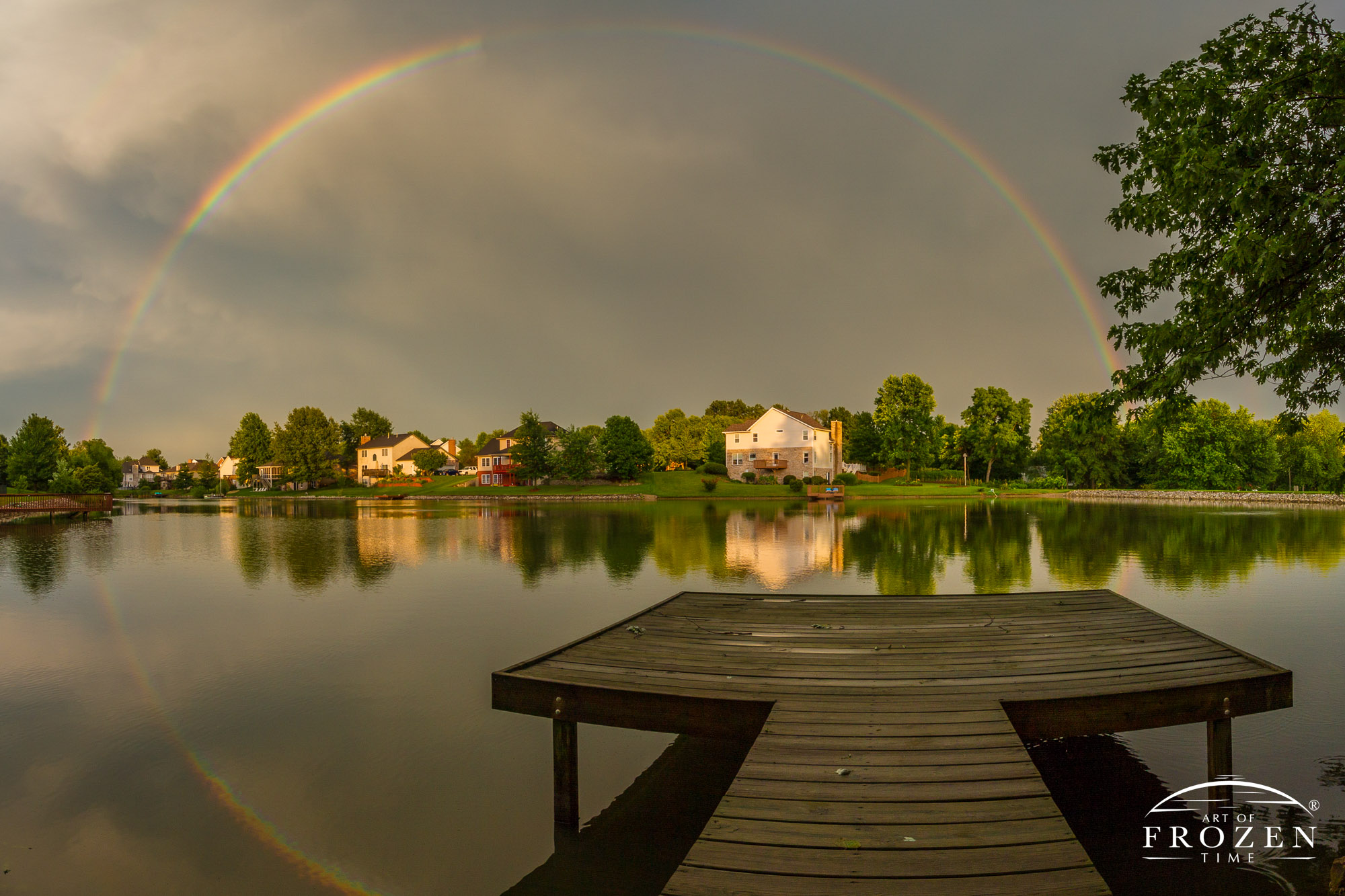 A full rainbow looking out from a small dock onto a pond where the surface waters reflected the optical delight created a full circle rainbow.