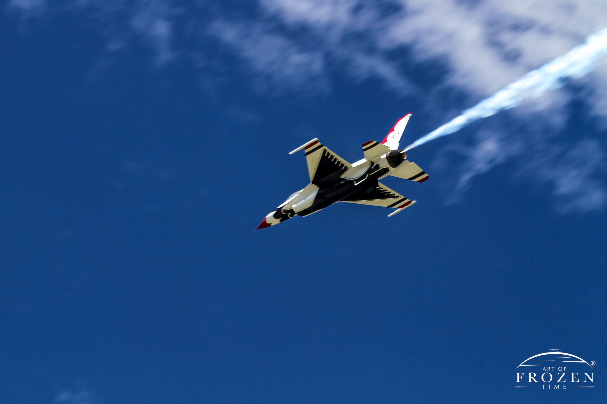 US Air Force Thunderbird making a high-speed pass with smoke on where the white contrast with the blue azure skies.