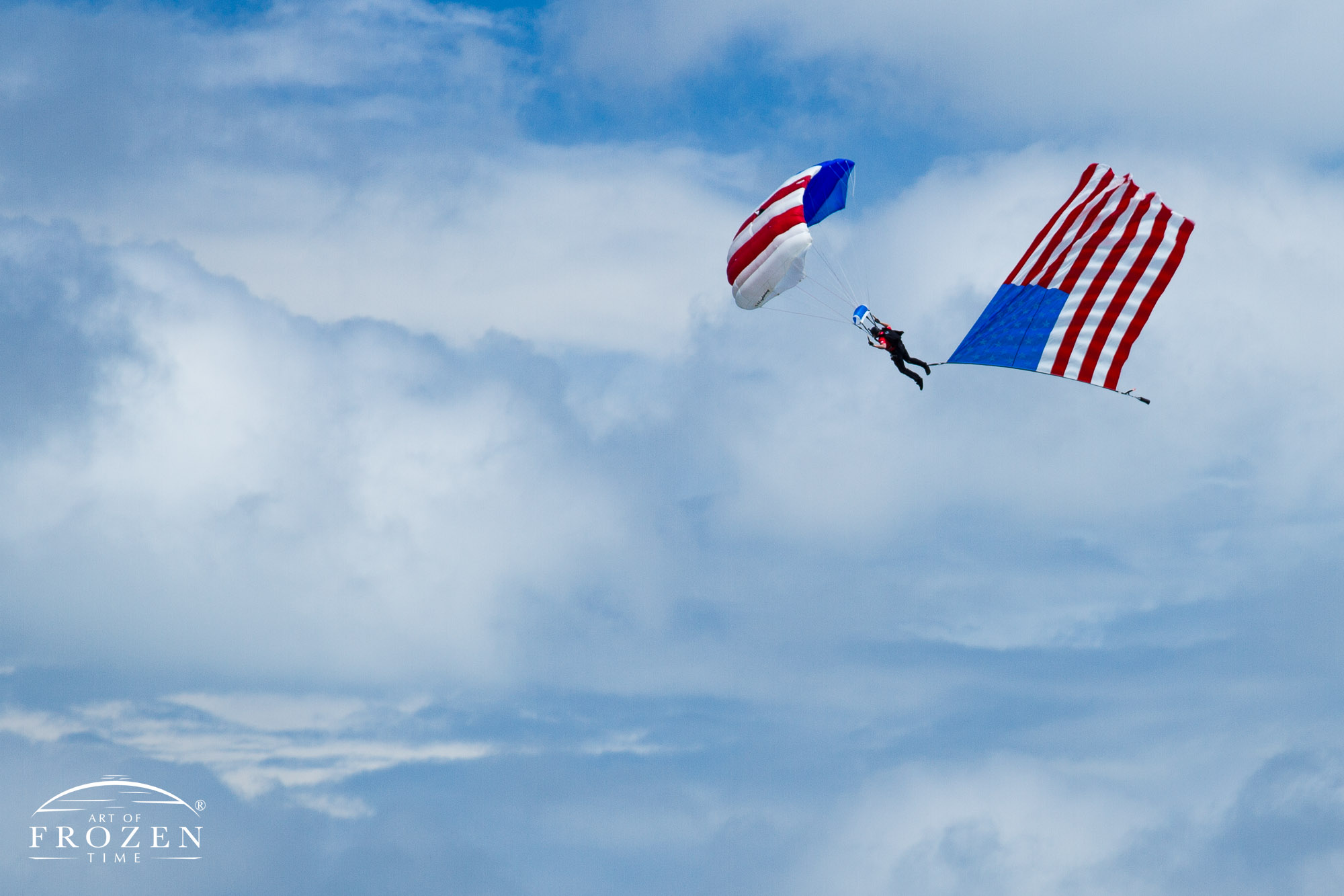 A red, white and blue envelope holds a parachutist with a US Flag floating from his foot as part of the opening festivities for the Lakeland Sun-n-Fun Airshow