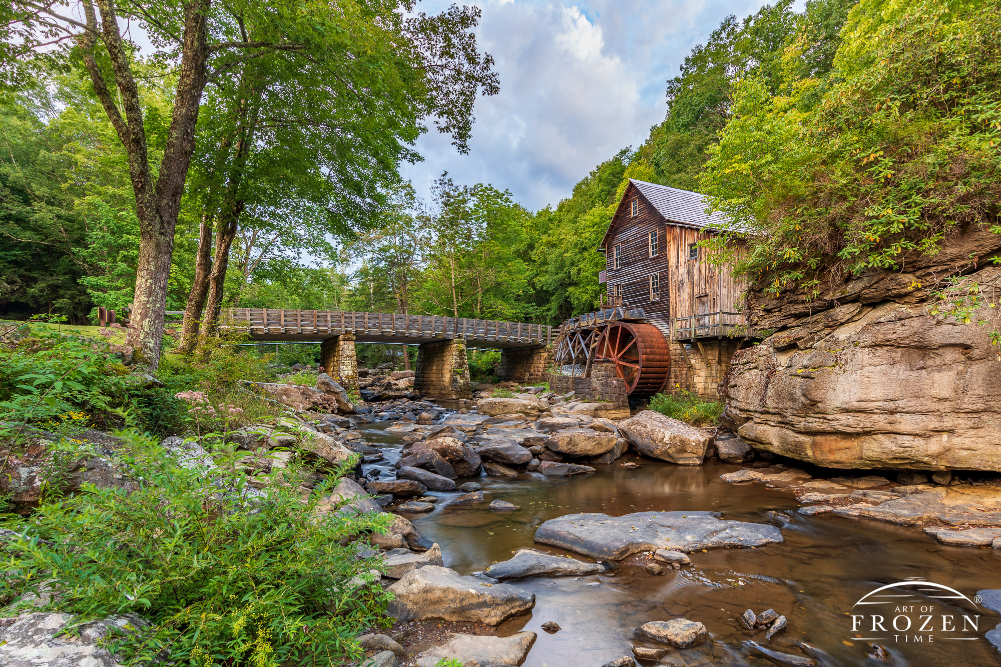 An enchanting West Virginia State Park scene where the Glade Creek Grist Mills stands in Glade Creek on a late summer evening as golden light paints the mill and surrounding trees