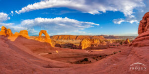 Panoramic image of Delicate Arch where golden light washes over the orange Entrada Sandstone