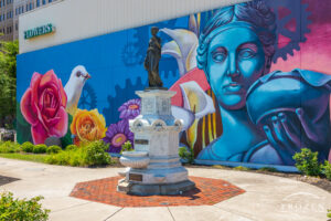 A colorful mural in Hamilton Ohio where the Greek subject of the mural matches the bronze sculpture mounted on a stone plinth.