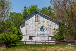 A white barn with chipping paint displaying artwork which commemorates the Miami County Ohio Bicentennial