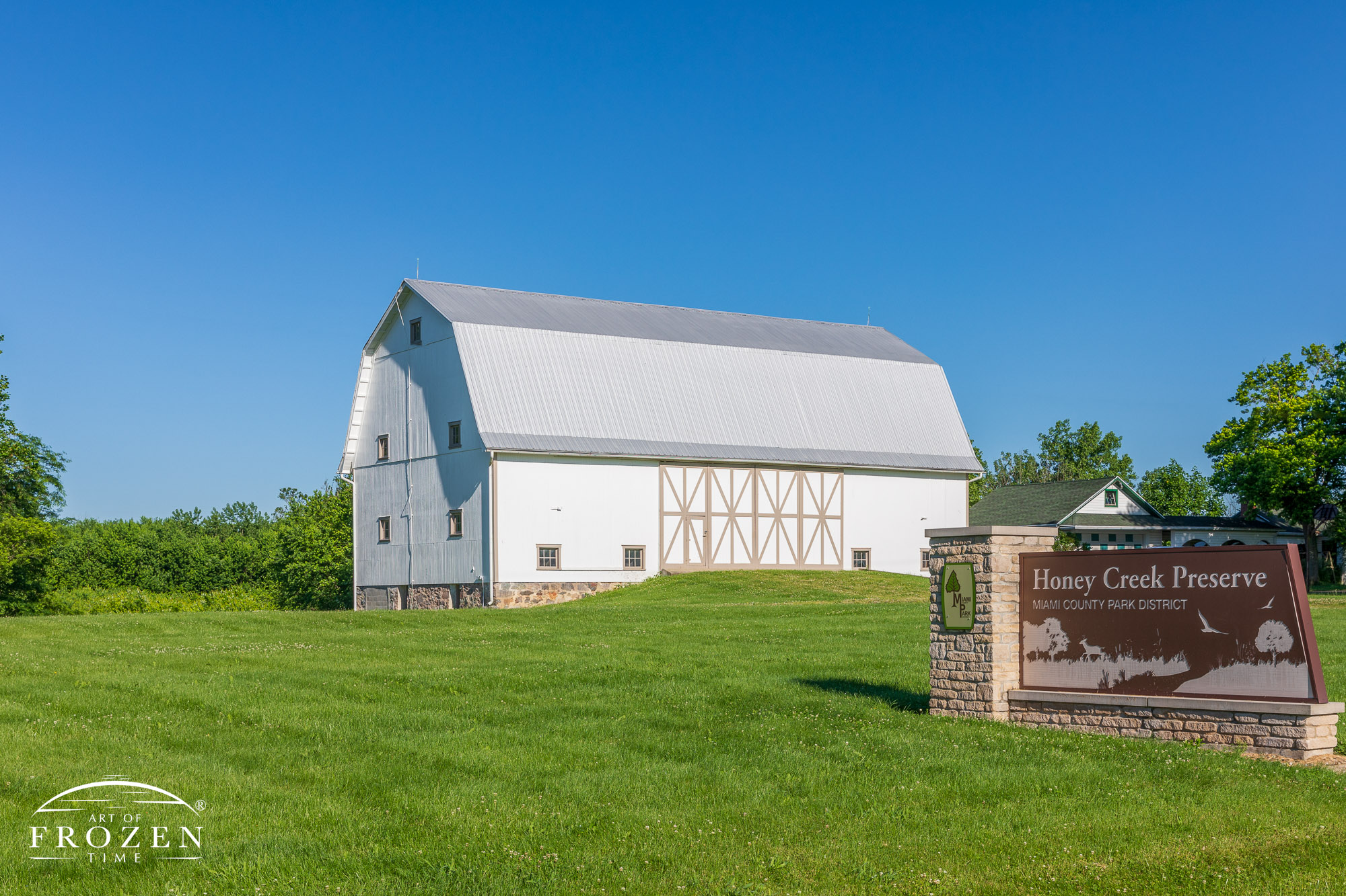 A white barn stands at the entrance of Honey Creek Preserve, outside Tipp City Ohio surrounding by lush vegetation and blue skies