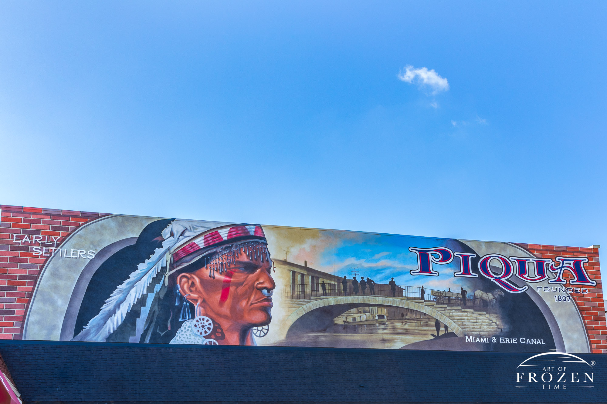 A colorful mural in Piqua Ohio featuring a Native American in ceremonial head wear and the Miami and Erie Canal