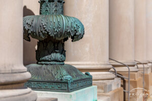 An intricate bronze lamp post surrounding by the clean lines of neoclassical stone columns.