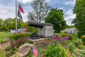 A canon residing a on block of granite surrounded by a flowerbed where the memorial honors one of the longest-serving veterans of the US Navy