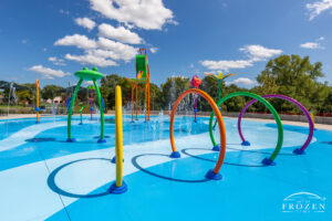 View of a colorful splash pad park in Springboro Ohio with water running under blue skies filled with white puffy clouds