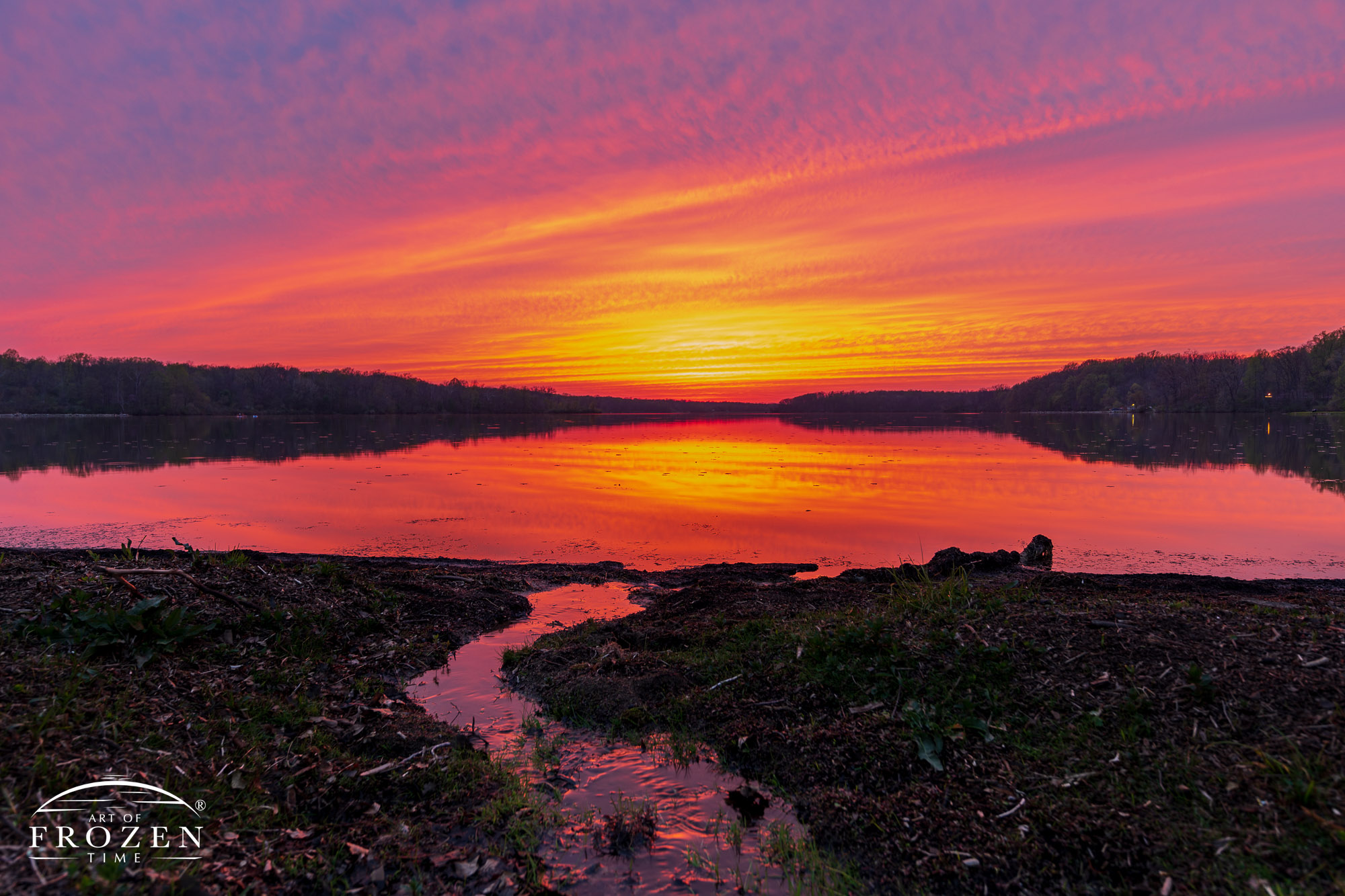 An orange dusky sunset during early spring where a small stream spills into Kiser Lake