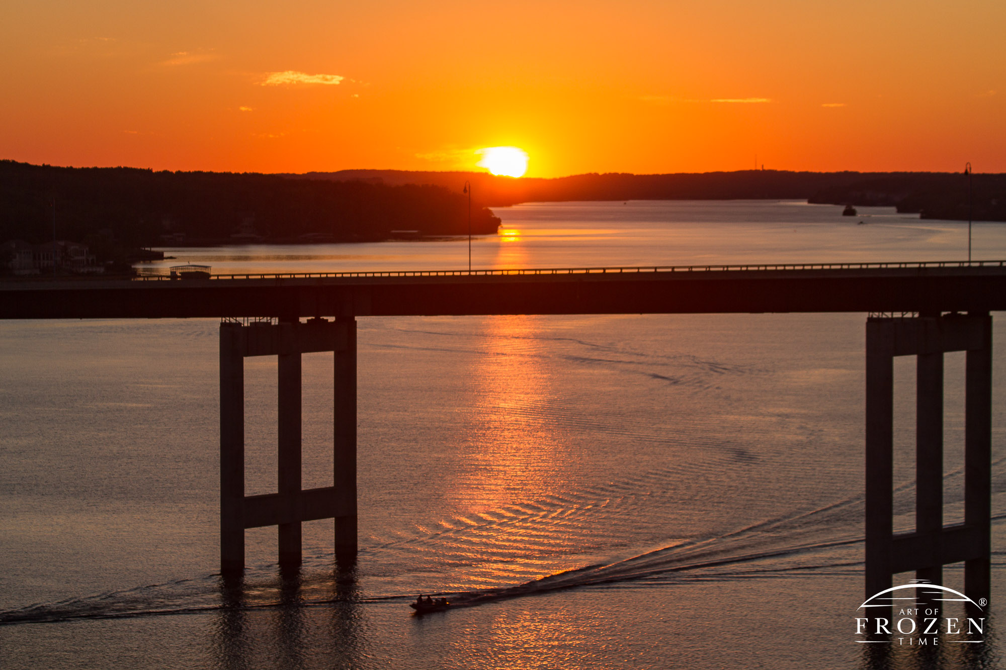 A sunset image of the Lake of the Ozarks Community Bridge as a boaters passed under the bridge as the sun dips below the western horizon