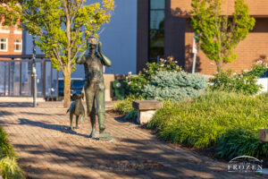 A two-part bronze sculpture featuring a barefoot boy marching and playing his harmonica as he is followed by an attentive dog