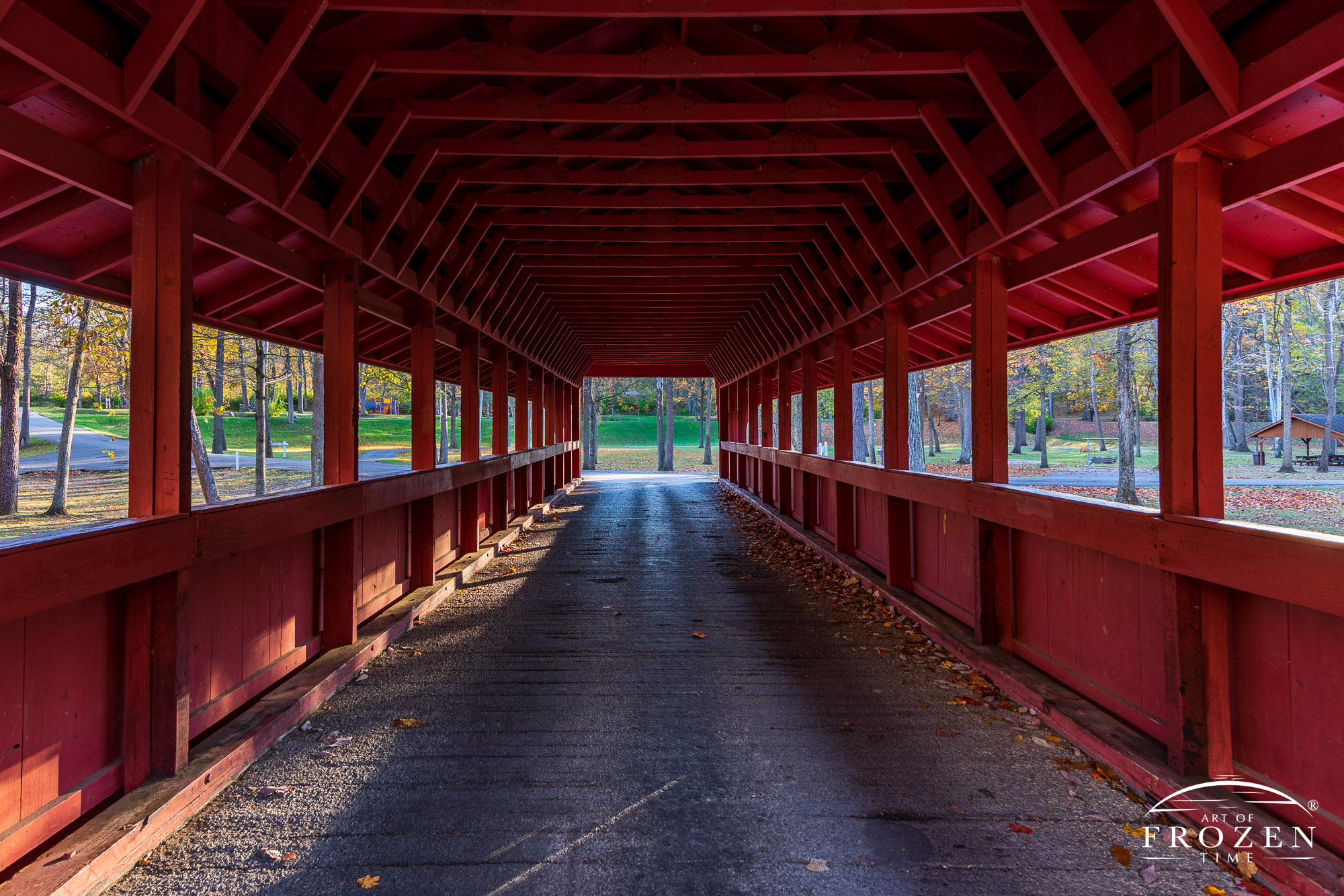 A wooden bridged with red paint spaces Tawawa Creek on a colorful autumn evening as the thinning leave barely block the setting sun and its golden light