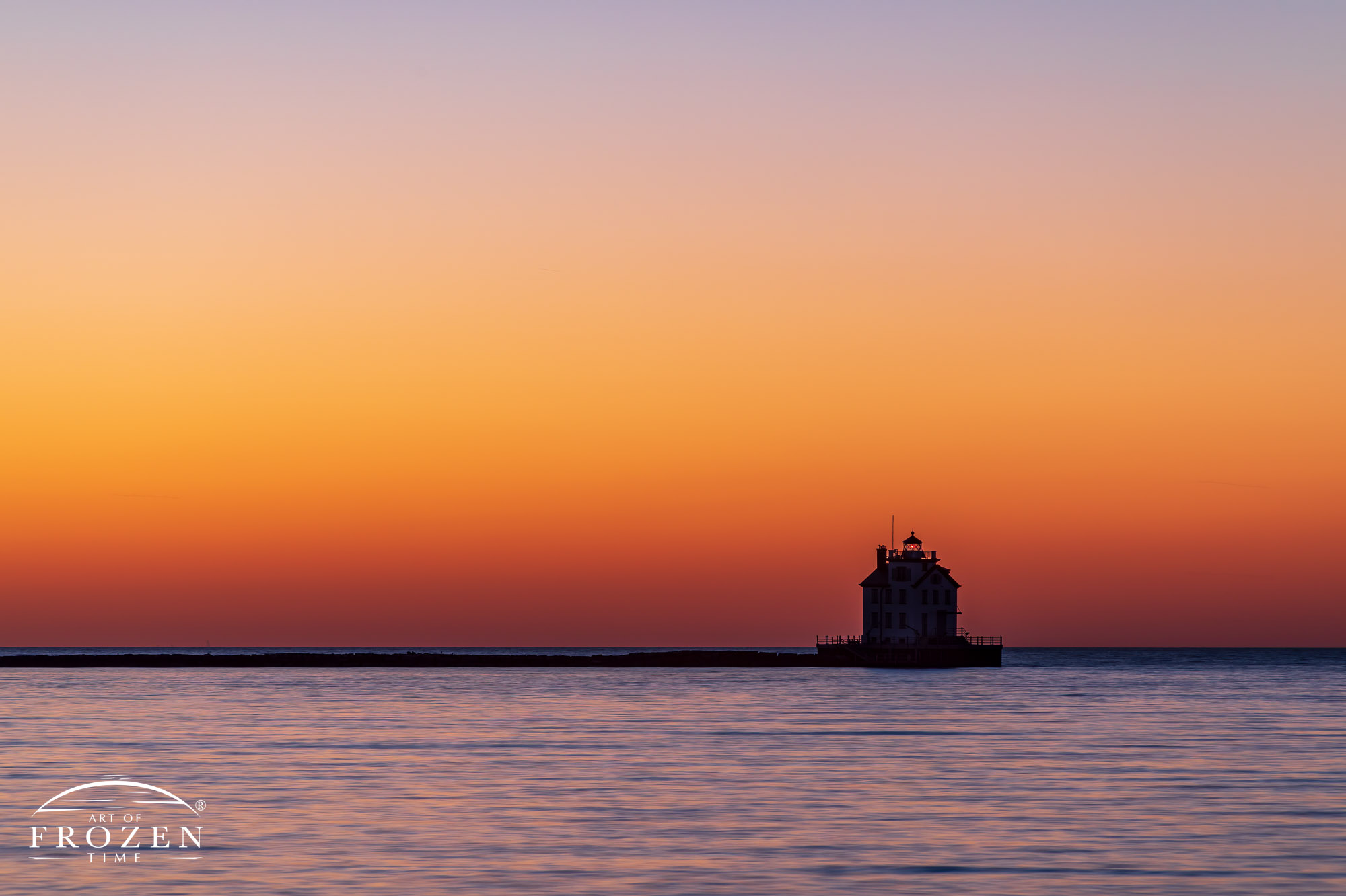 Twilight over Lorain Lighthouse as the clear Lake Erie horizon takes on varying orange hues while the lake surface refracts light from the darker blue skies above.