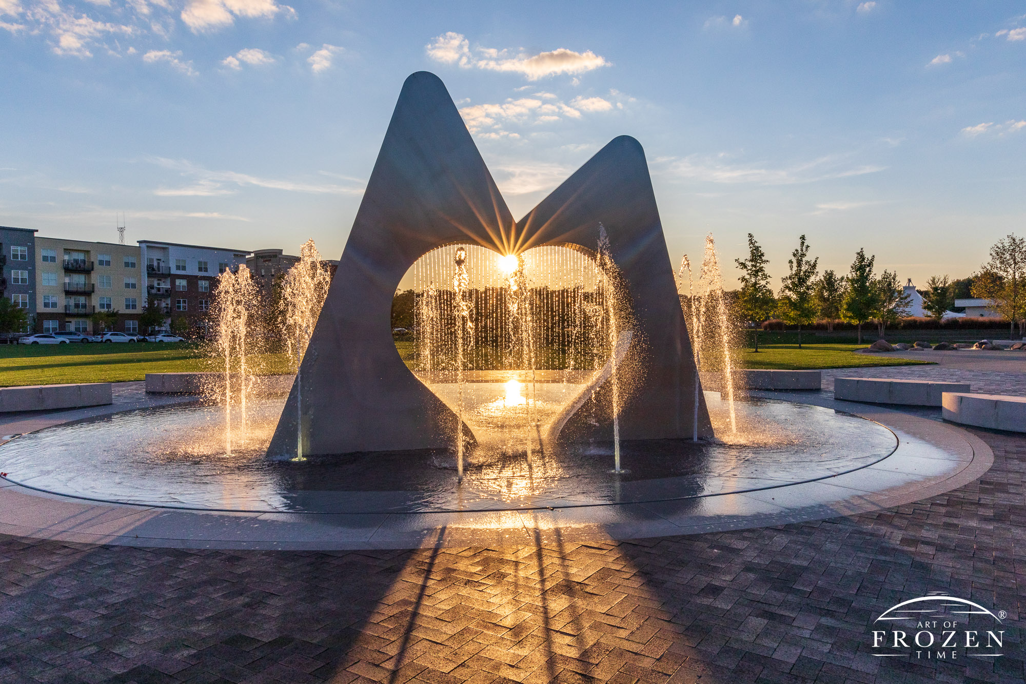 An evening image of Marcum Park Fountain, Hamilton Ohio, where the fountain glistens in the golden light from the setting sun