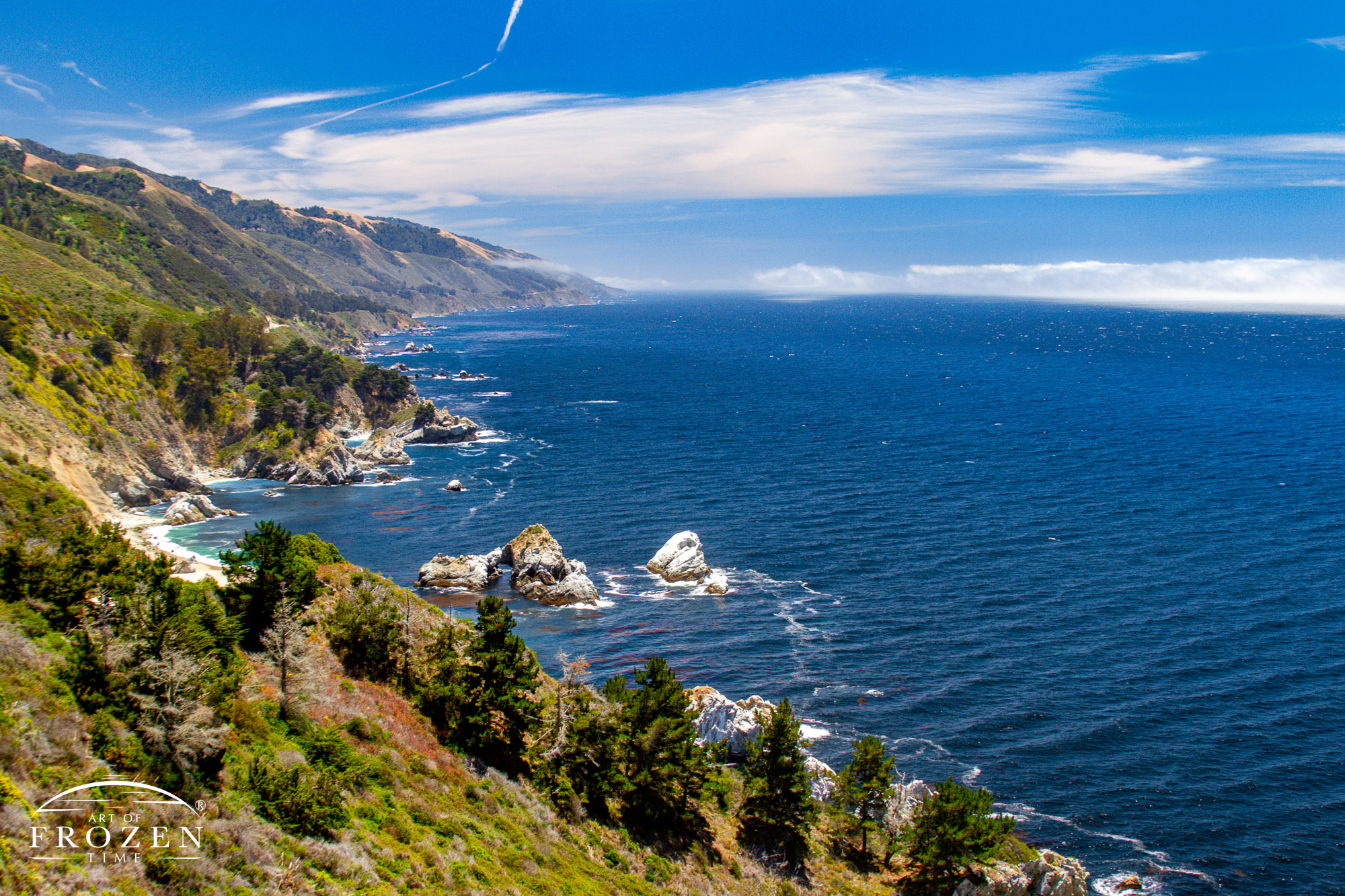 The McWay Rocks along California's Big Sur on a gorgeous June day where the deep blue water washes ashore and distant sea fog makes its way to the rocky coast