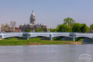 The Great Miami River runs under Troy Ohio’s Adams Street bridge as the Miami County Courthouse resides under blue skies