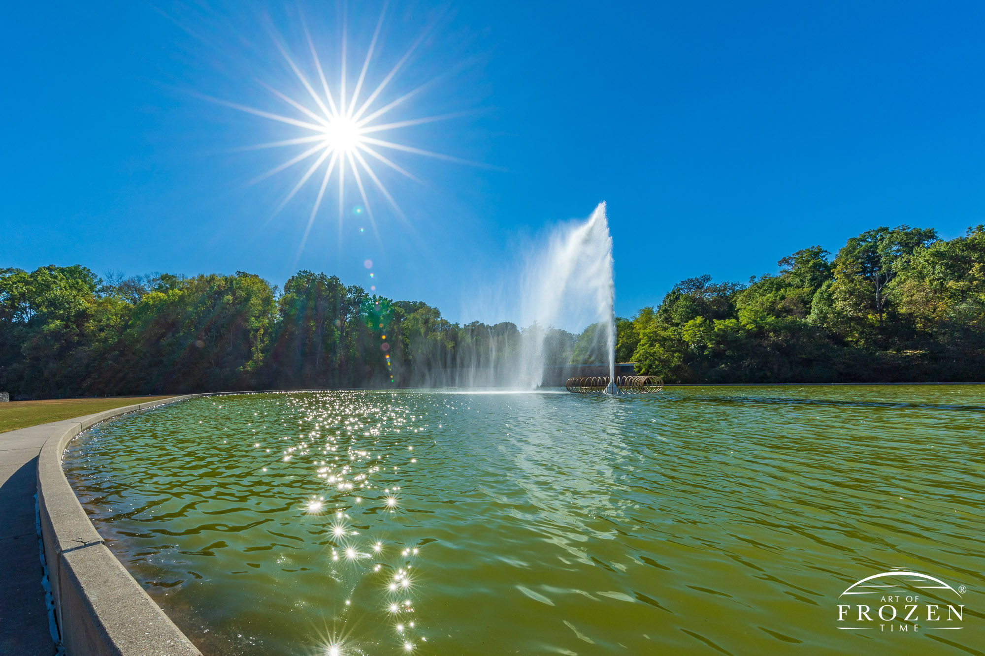 As a fountain casts streams of water into the air, the brilliant sun hanging the blue azure skies backlit the water spray