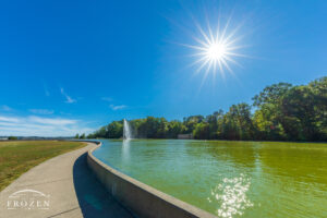As a fountain casts streams of water into the air, the brilliant sun hanging the blue azure skies backlit the water spray