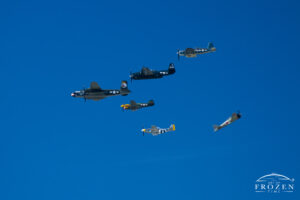 A formation of various WWII aircraft flying in formation as a re-enactment WWII Japanese zero zooms past from the opposite direction