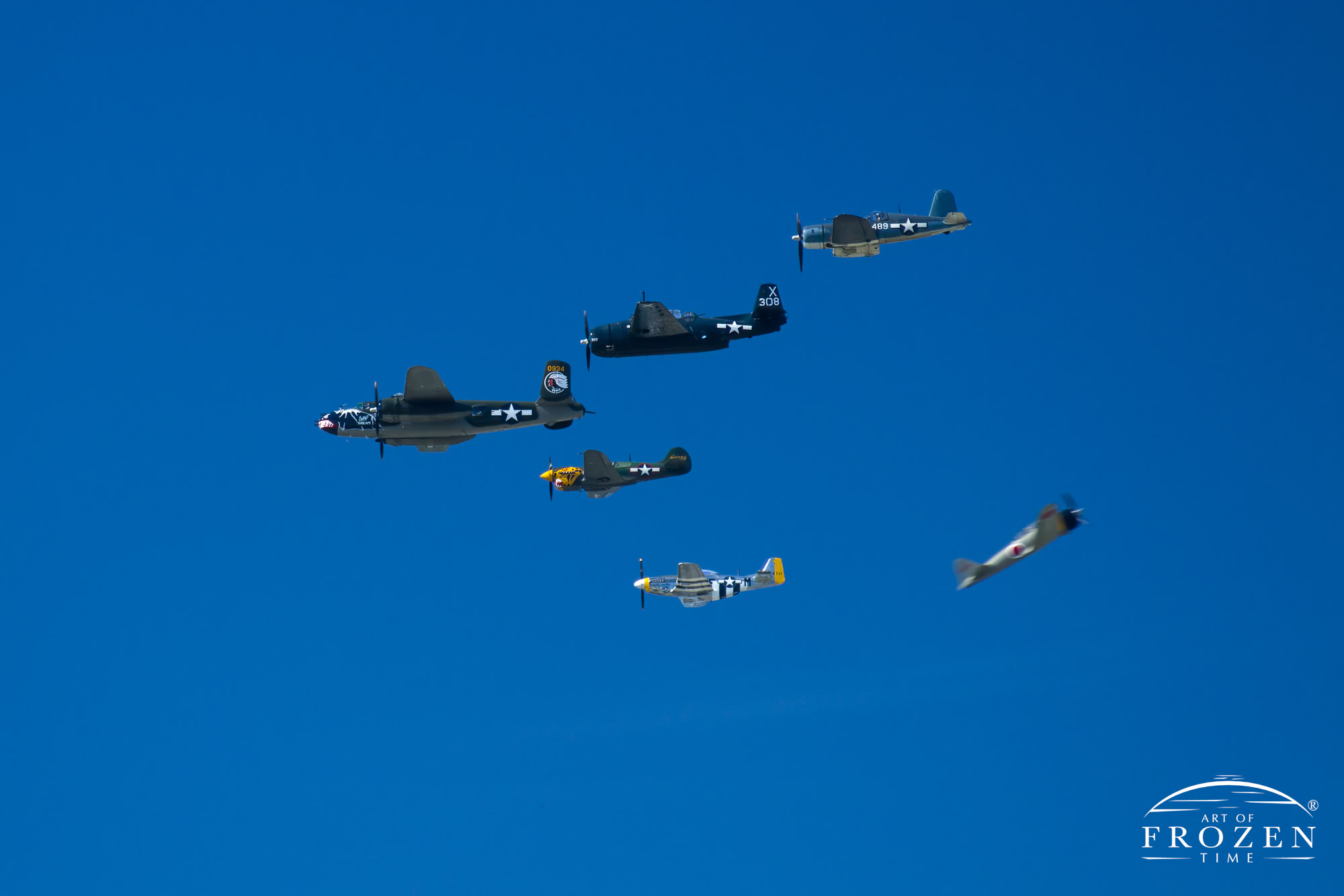 A formation of various WWII aircraft flying in formation as a re-enactment WWII Japanese zero zooms past from the opposite direction