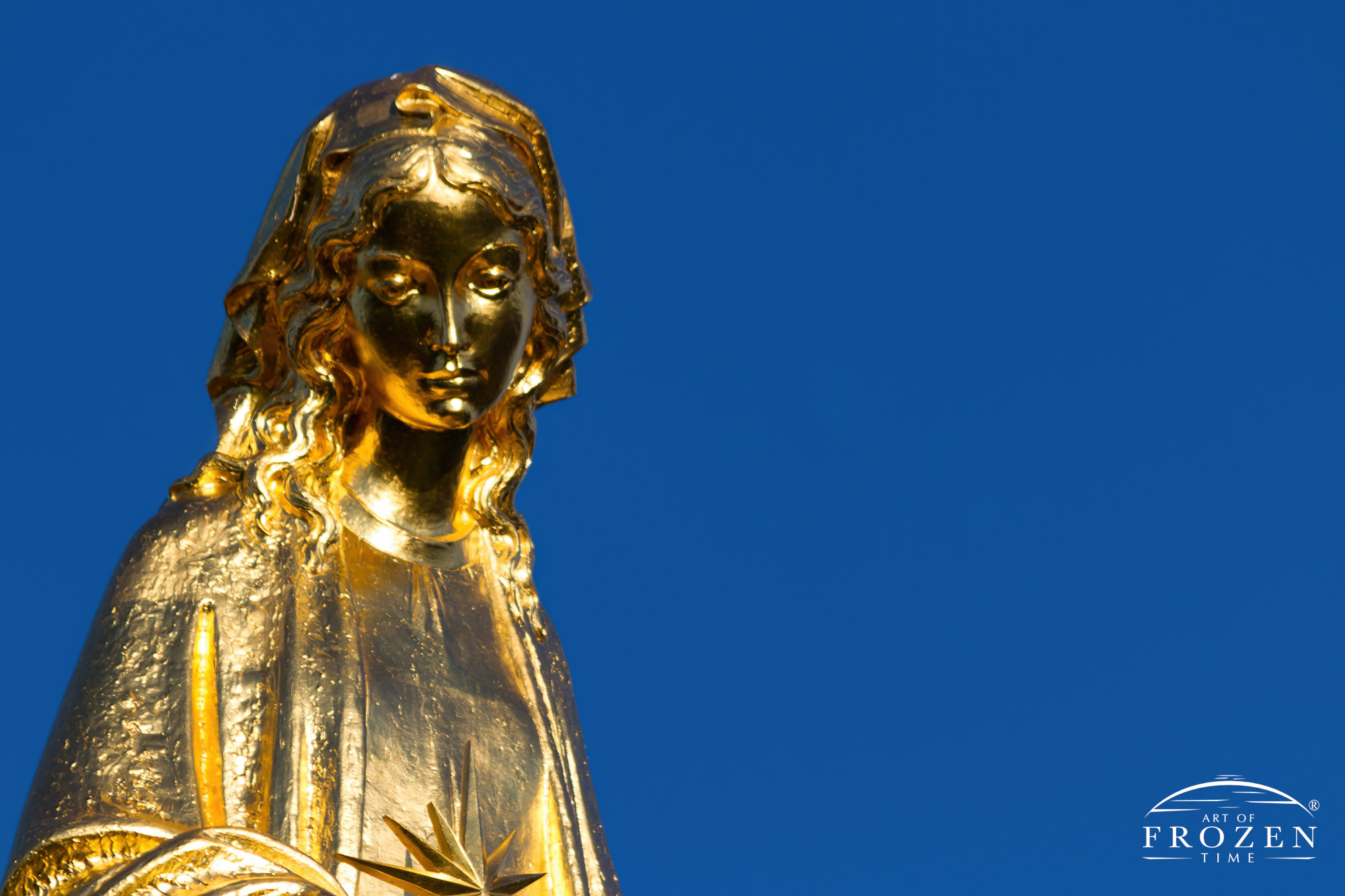 A golden embossed statue of the Virgin Mary on top the steeple of Our Lady of the Lake Catholic Church on a clear blue day