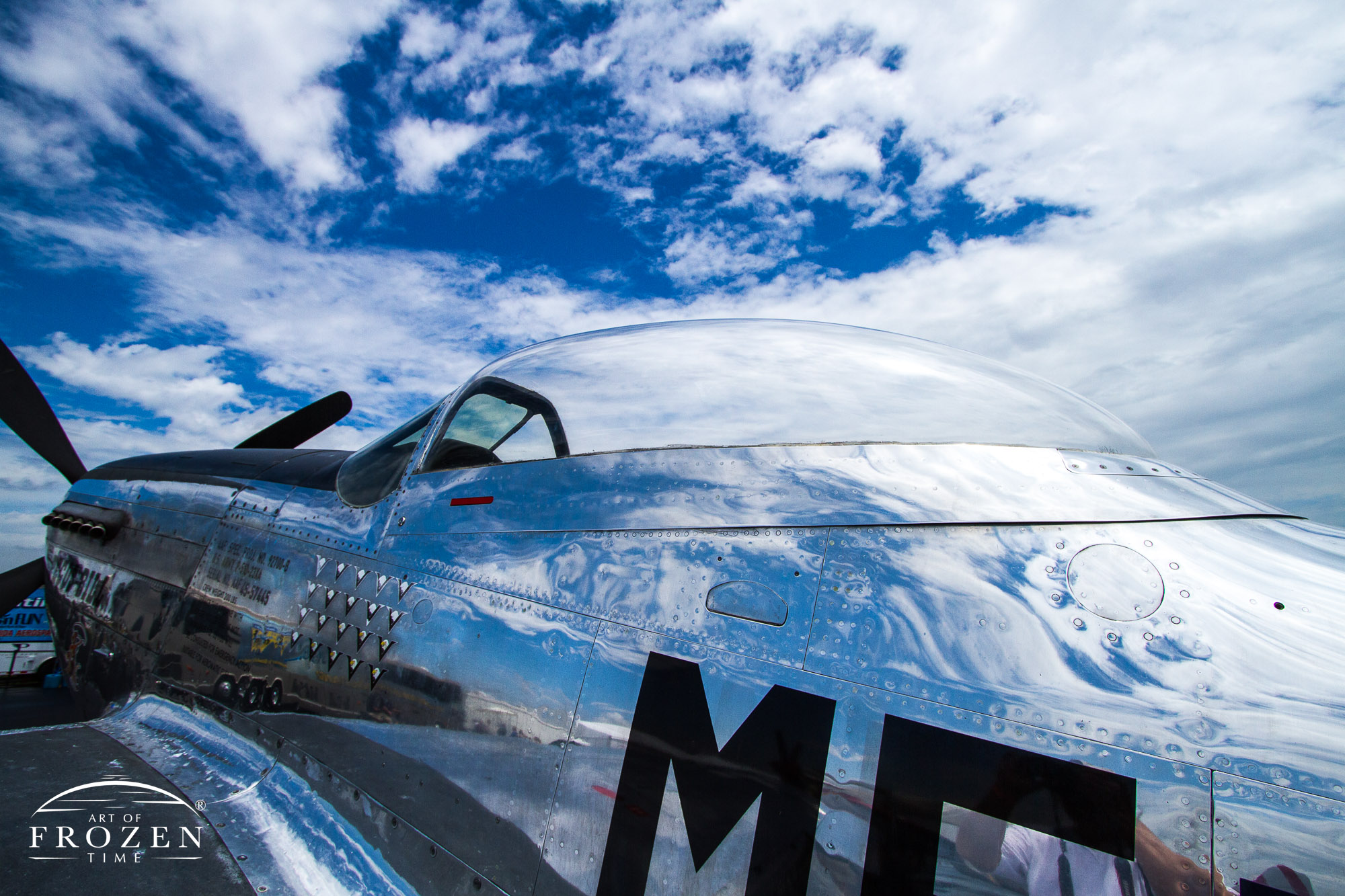 A cropped image of a P-51 Mustang fuselage where the highly polished finish reflects the partly cloudy sky above.