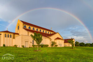 A full rainbow hands over St Clare of Assisi, O'Fallon Illinois as storm clouds yield to sunshine at sunset casting golden light over the church grounds