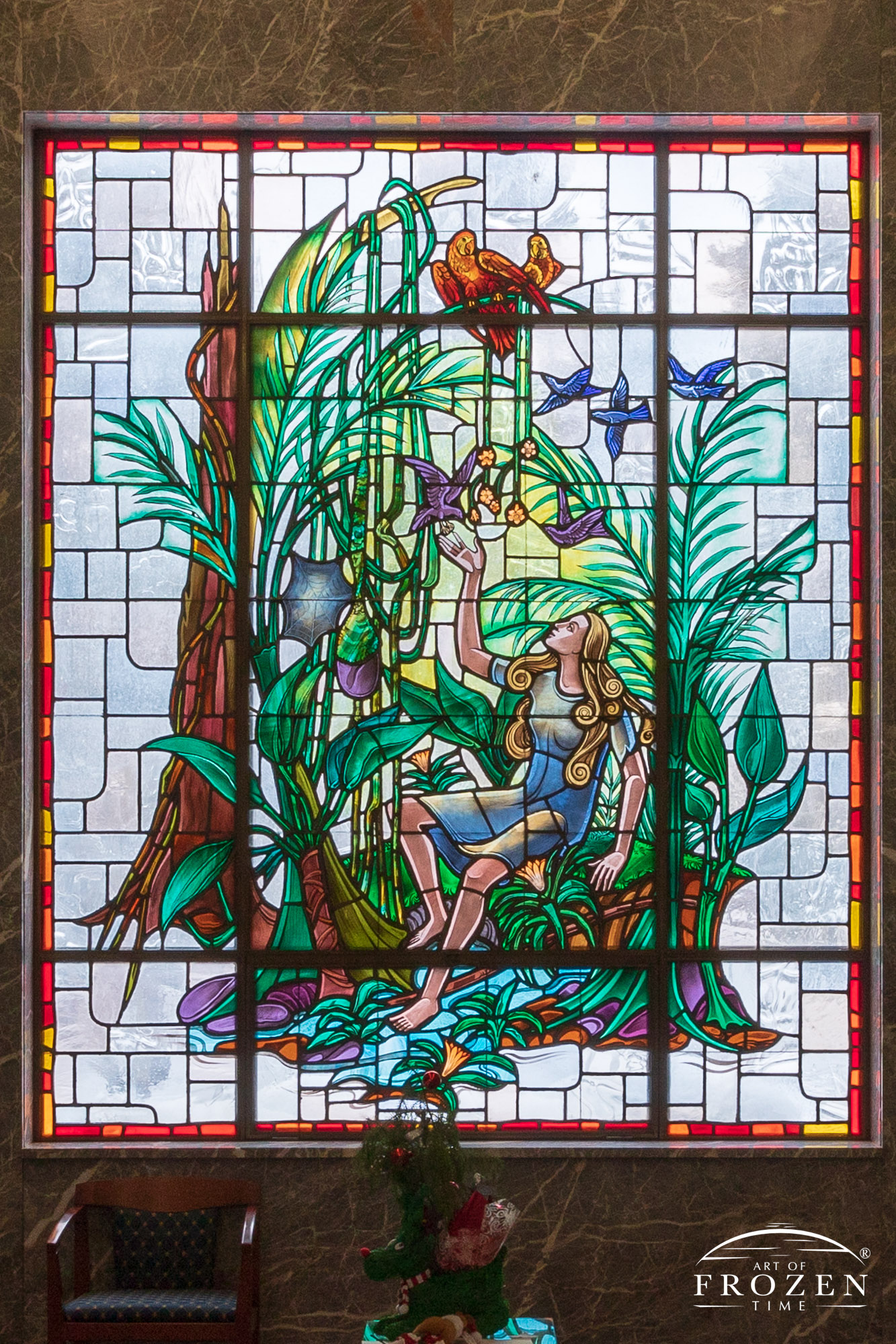 Historic stained-glass windows created by Louis Comfort Tiffany featuring his opalescent glass depicting a young lady sitting in a garden reaching towards birds.