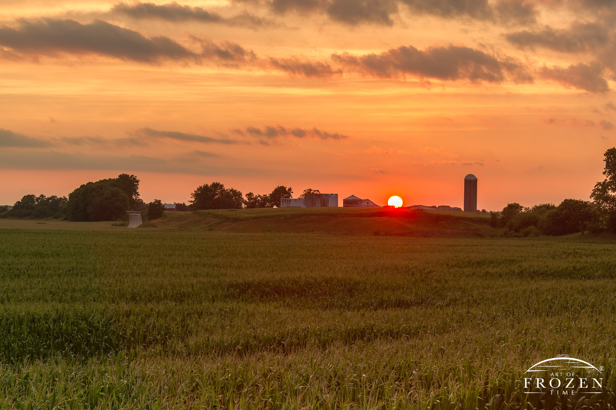 A sunset over a Scioto Valley farm where the sun is a bright orange ball before it sinks below the horizon whose bright light created a silhouette of the Ohio farmstead