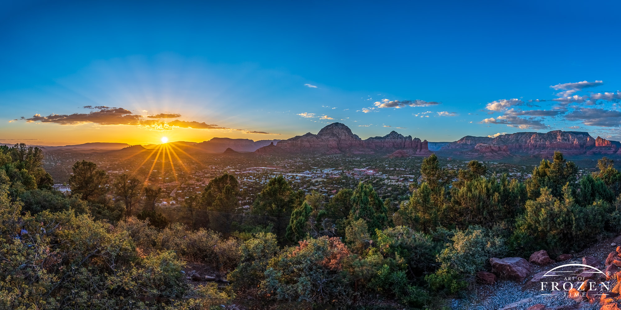 Panoramic sunset from Sedona Airport Scenic Lookout where the sun’s rays paint Red Rock Country in golden light and a sunburst appears over the distant Cockscomb Rock formation and Black Mountain