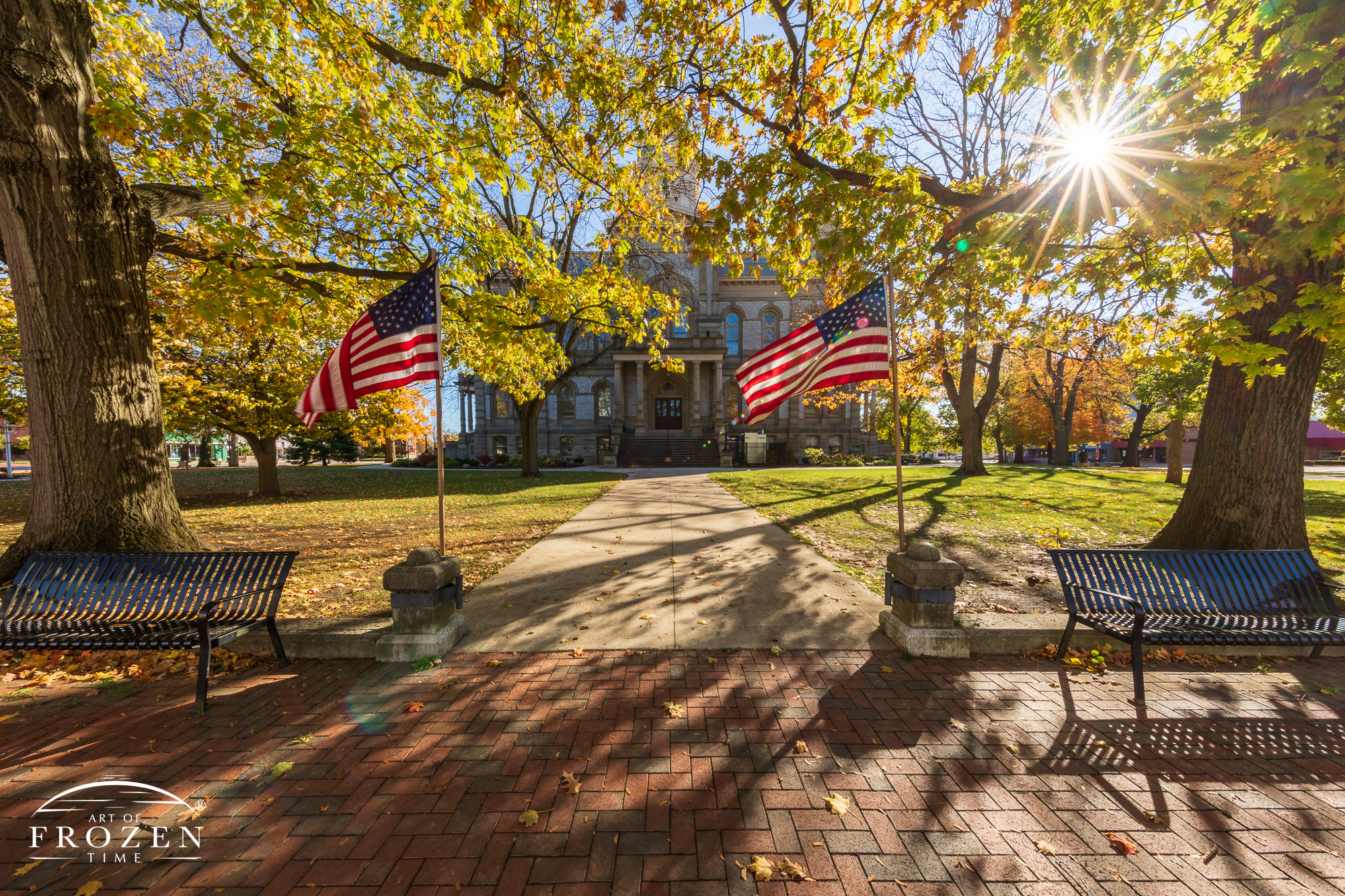 A view of the county courthouse in Sidney, Ohio on a fall evening where the golden light from the sun backlights the fall leaves and US Flags flapping in the wind