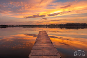 A simple image of a dock extended into a calm mirror-finish lake when a colorful and moody sunset takes to the Illinois sky