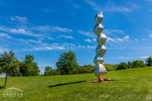 A tall stainless steel sculpture where the six stacked Octahedrons appear to spiral skyward under blue skies