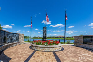 An impressive Veterans memorial with neat pavers, colorful floors and etched granite panels all stand under fluttering flags.
