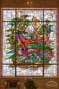 Historic stained-glass windows created by Louis Comfort Tiffany featuring his opalescent glass depicting a prince kneeling before a stag which holds a crucifix between its antlers.