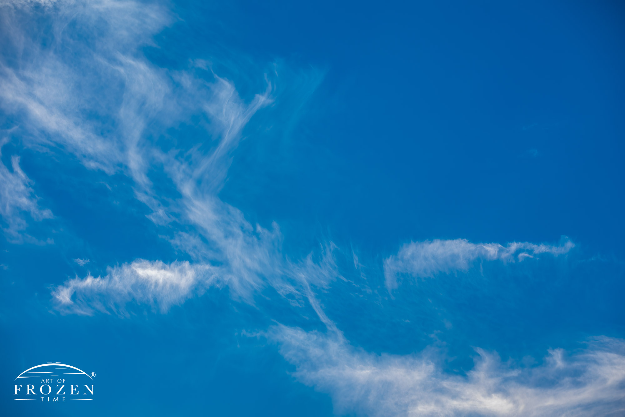 A view of high-altitude clouds blown into wispy swirls and shapes against the blue azure canvas.