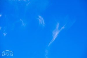 A view of high-altitude clouds blown into wispy swirls and shapes against the blue azure canvas.
