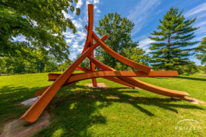 A bright orange sculpture of eight curved steel I-beams placed in a mix of horizontal and vertical positions